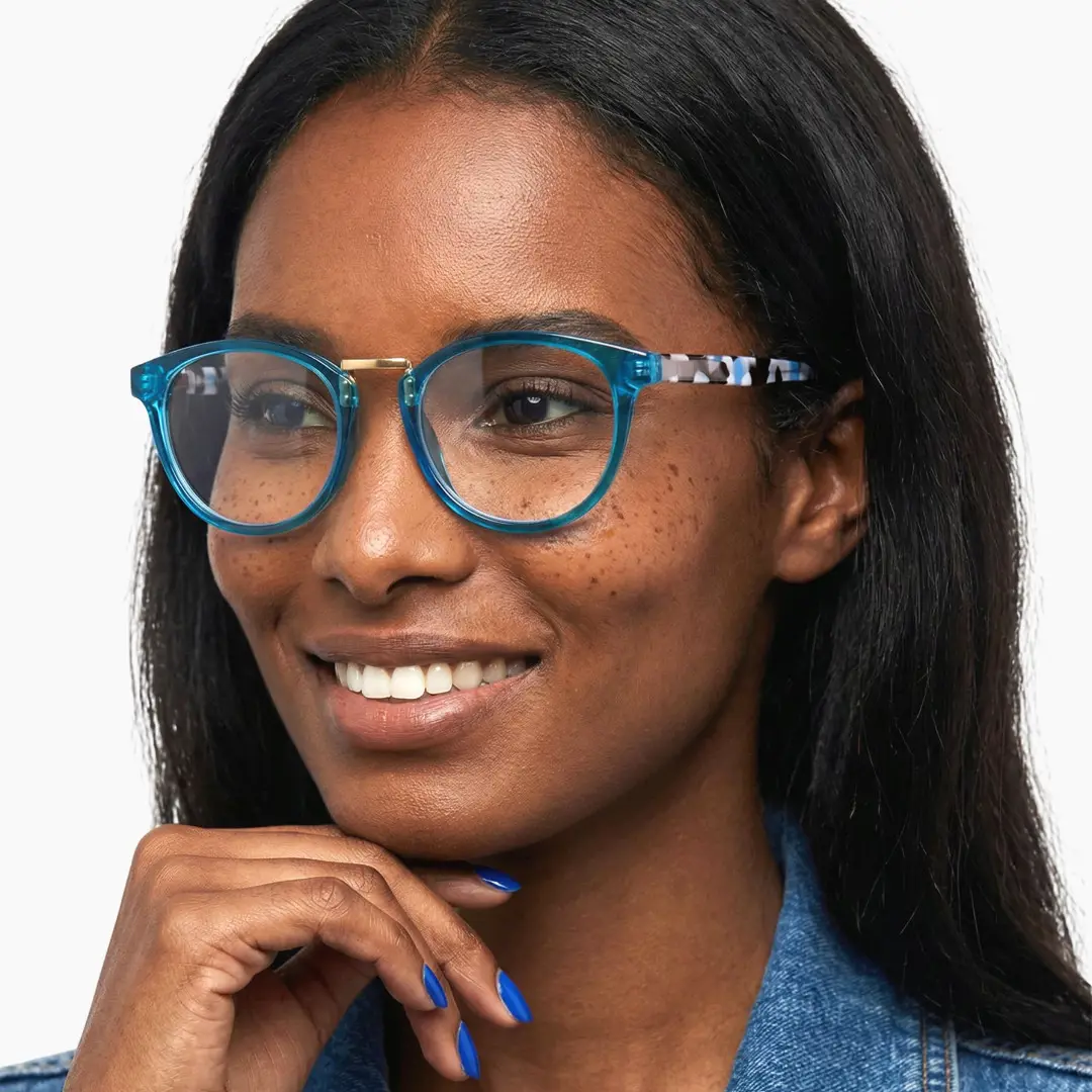 Slightly angled view of female wearing blue oval eyeglasses, hand touching chin, smiling, OP0222311
