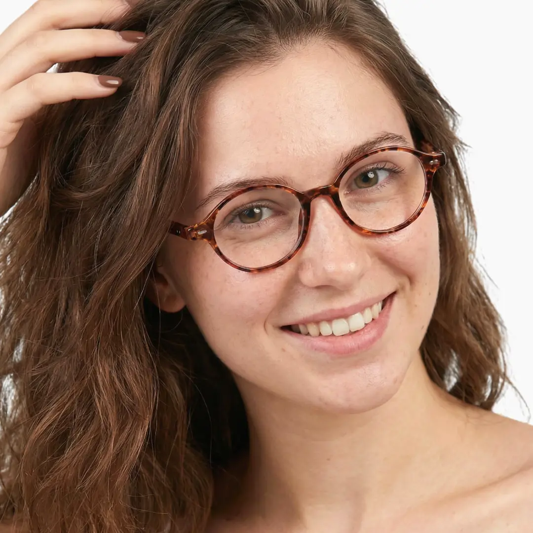 Slightly angled view of female wearing tortoise oval eyeglasses, hand in hair, smiling, OR0082406