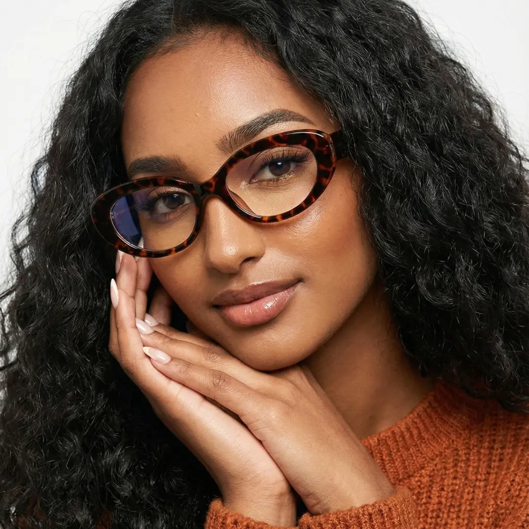 Face close-up view of female wearing y2k tortoise oval eyeglasses, hand near face, natural smile, OR0132510