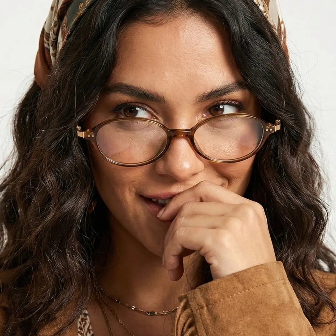 Front view of female wearing y2k brown oval eyeglasses, resting chin on hand, natural smile, OR0272410