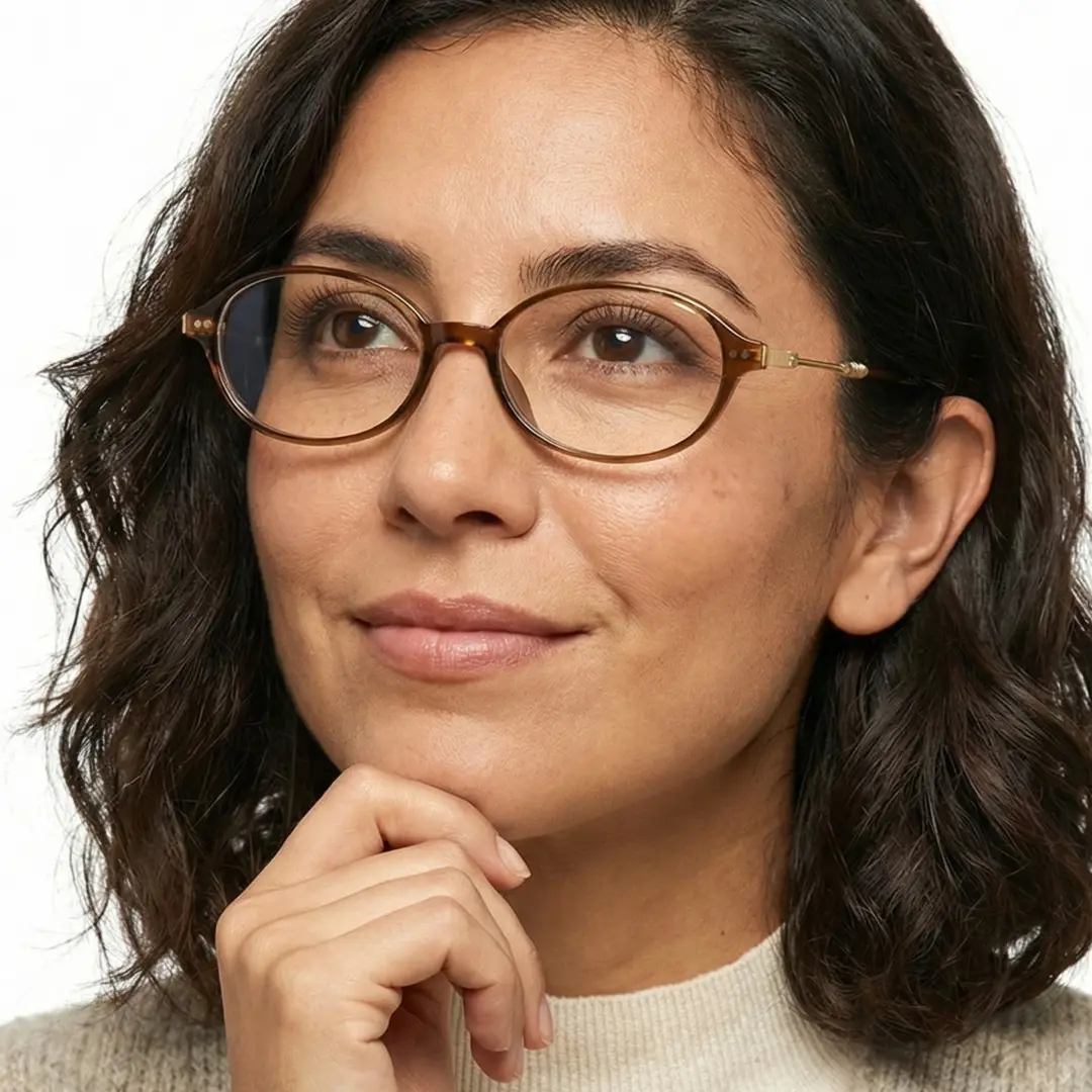 Looking away view of female wearing y2k brown oval eyeglasses, resting chin on hand, soft smile, OR0272410