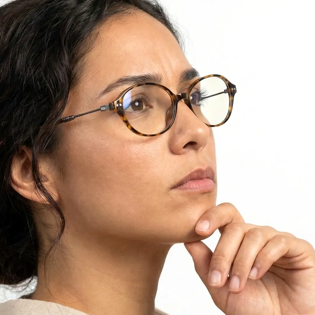 Profile view of female wearing tortoise oval eyeglasses, resting chin on hand, thoughtful expression, OR0272410