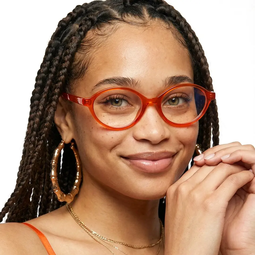 Front view of female wearing orange oval eyeglasses, hand near face, natural smile, OR0312402