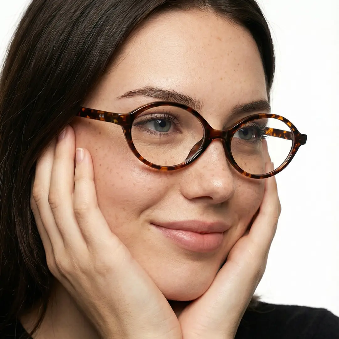 Three-quarter view of female wearing y2k tortoise oval eyeglasses, resting chin on hand, natural smile, OR0312402