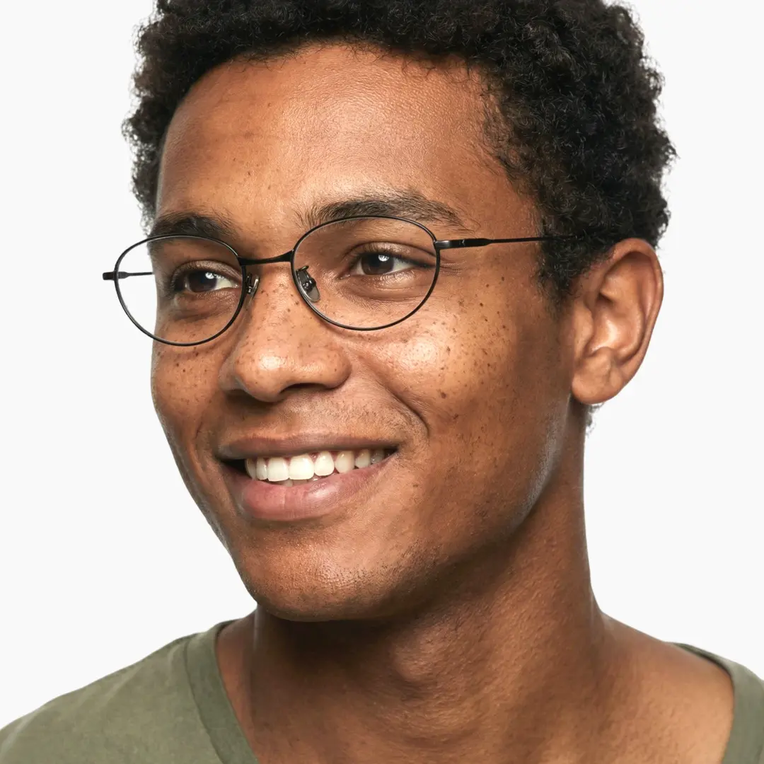 Three-quarter view of male wearing y2k black oval eyeglasses, natural smile, OT0072501