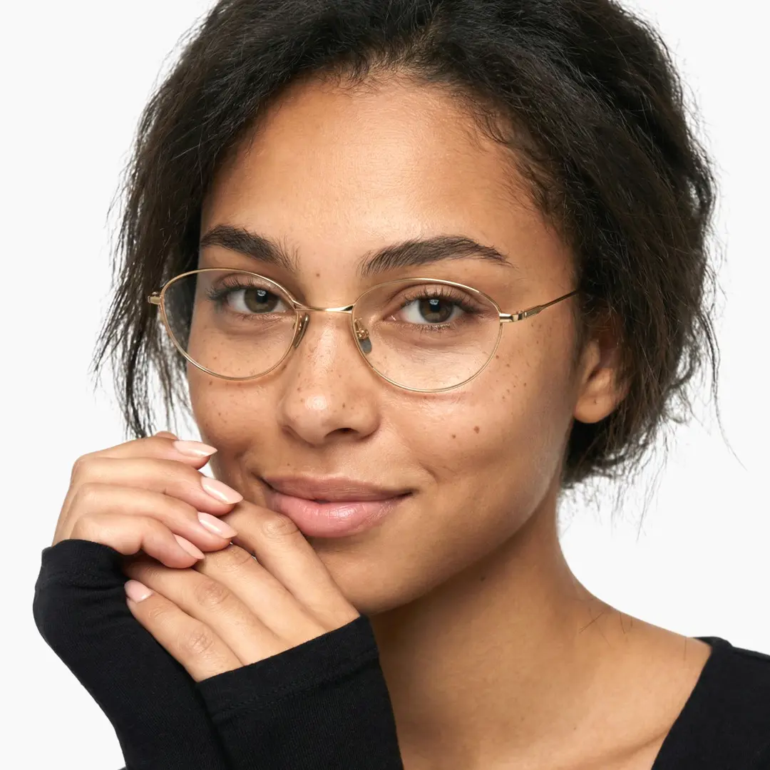Front view of female wearing y2k gold oval eyeglasses, hand near face, friendly smile, OT0072501