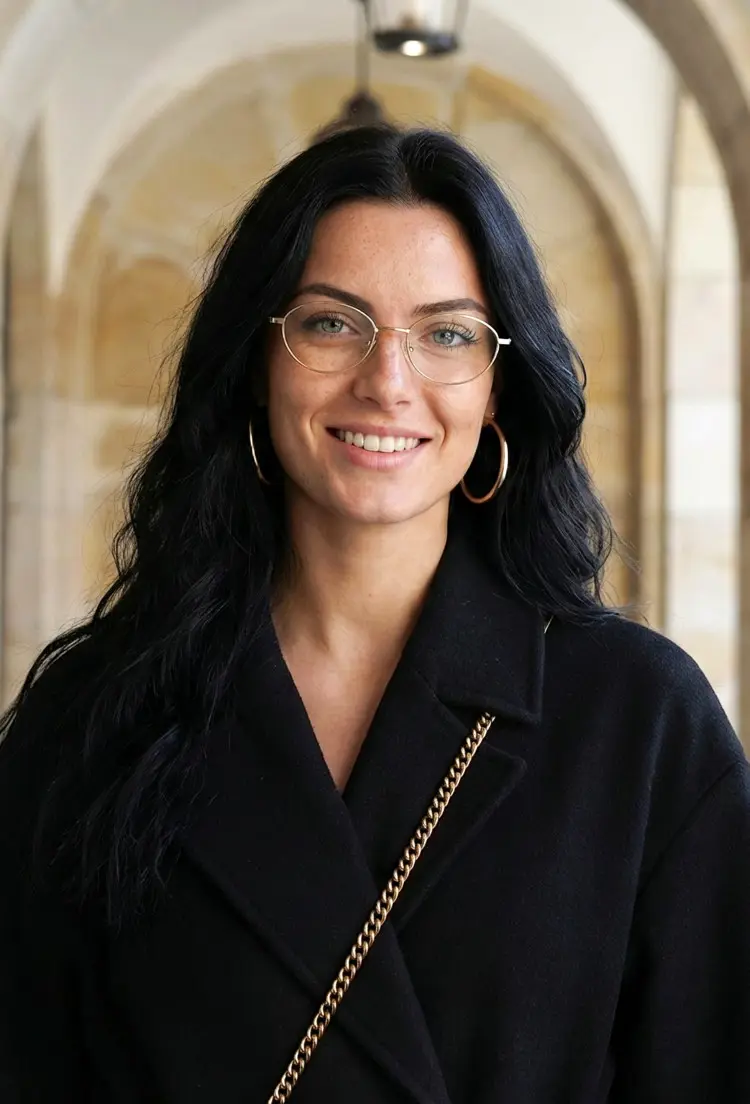 Female model wearing everyday gold oval titanium eyeglasses in a sunlit stone archway corridor. SPU: OT0072501