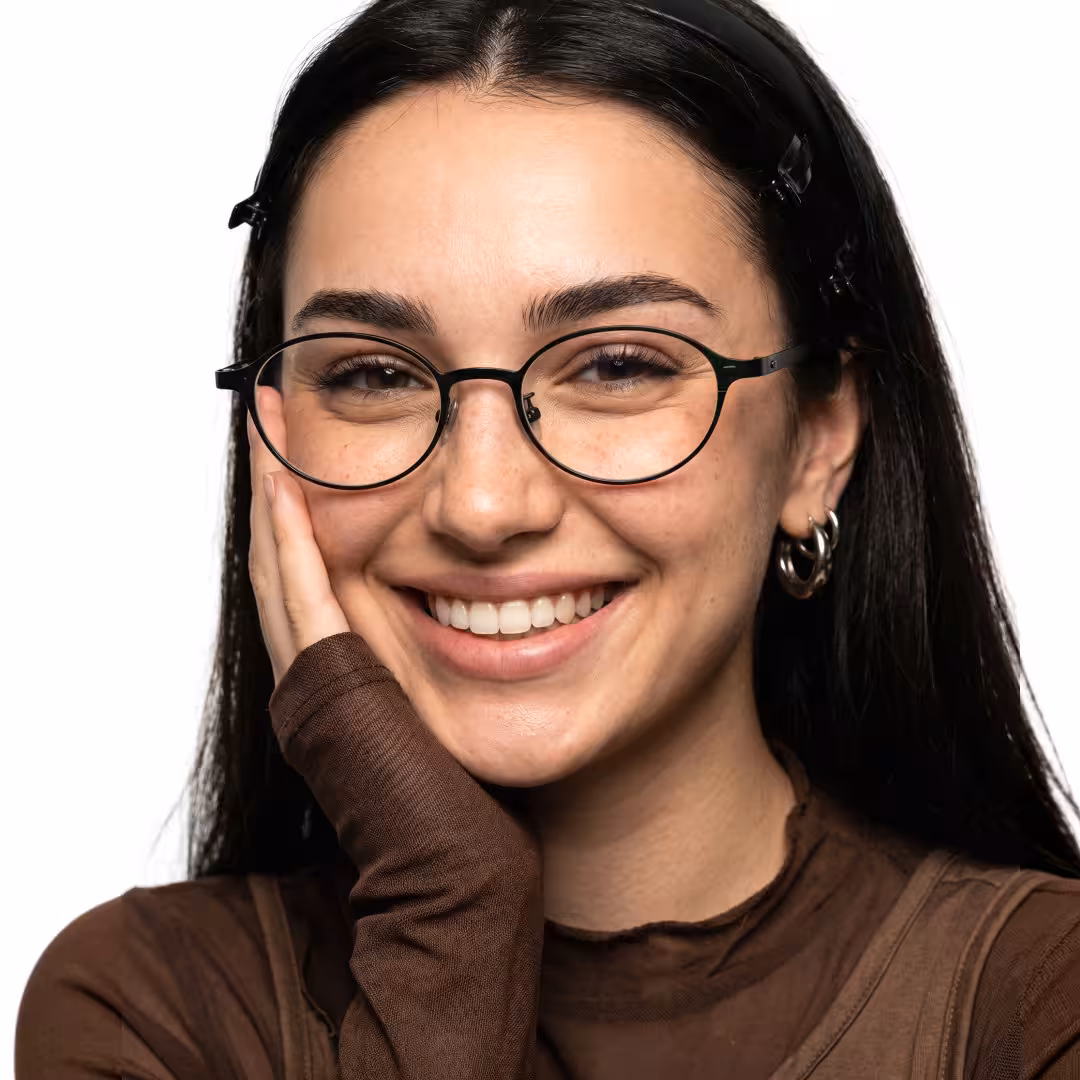 Close-up view of female wearing y2k black oval eyeglasses, hand near face, smiling, OT0132412