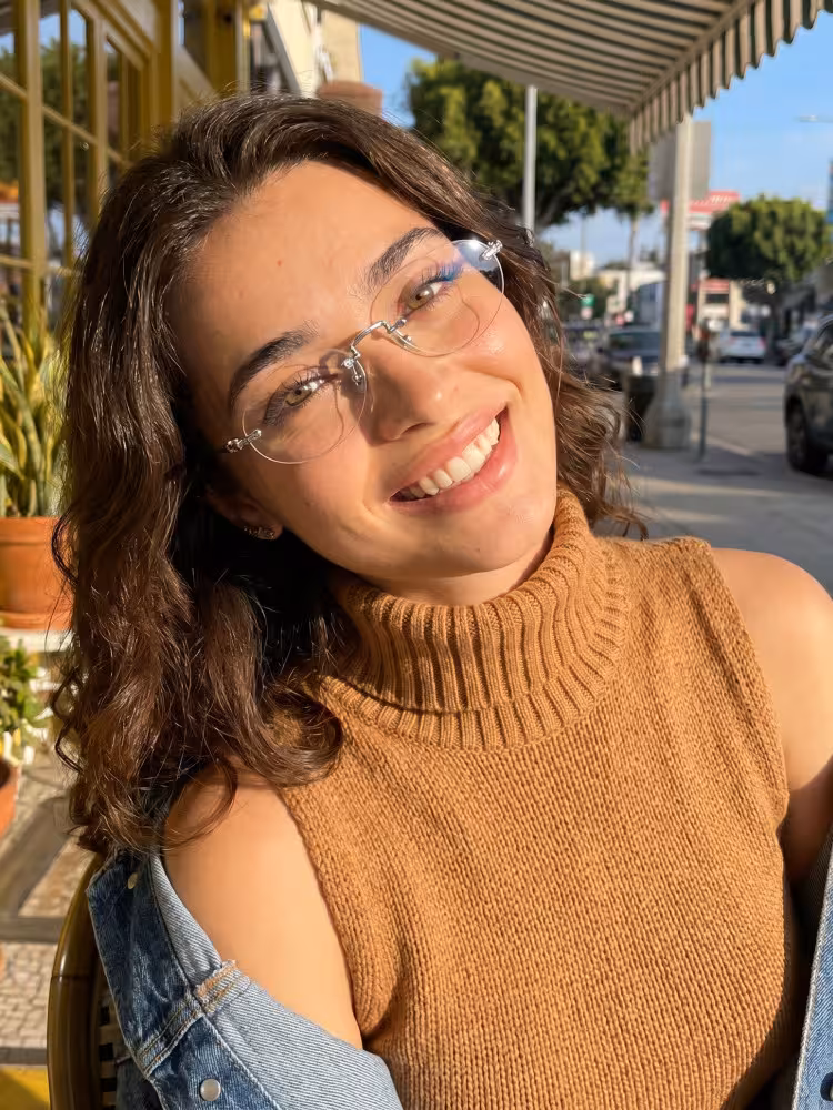 Female model wearing fashion silver oval titanium eyeglasses sitting at a sunny outdoor cafe. SPU: OT0142604