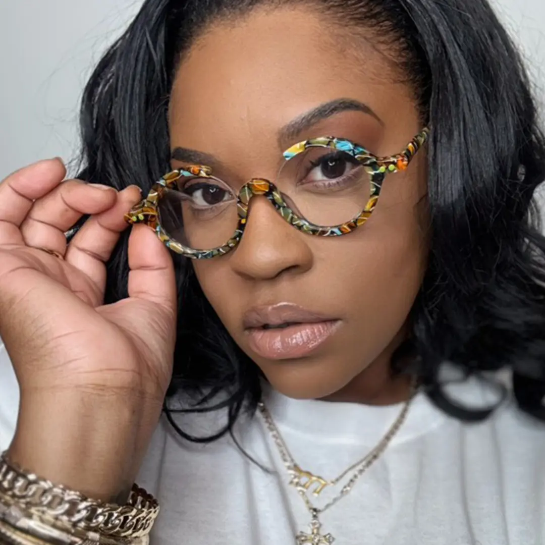 Slightly angled view of female wearing multicolor round eyeglasses, holding glasses, neutral expression, RA0022212