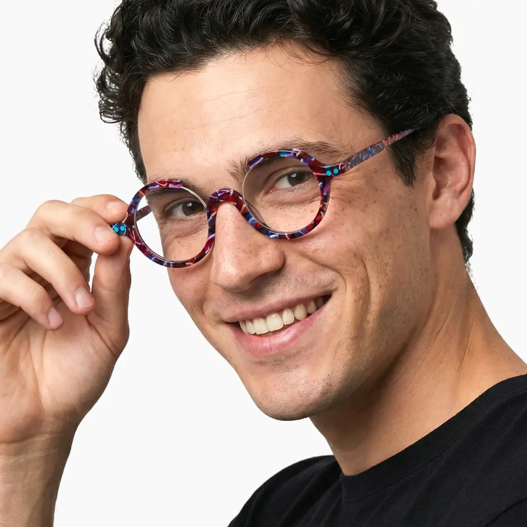 Over-the-shoulder view of male wearing red tortoise round eyeglasses, holding glasses, smiling, RA0022212