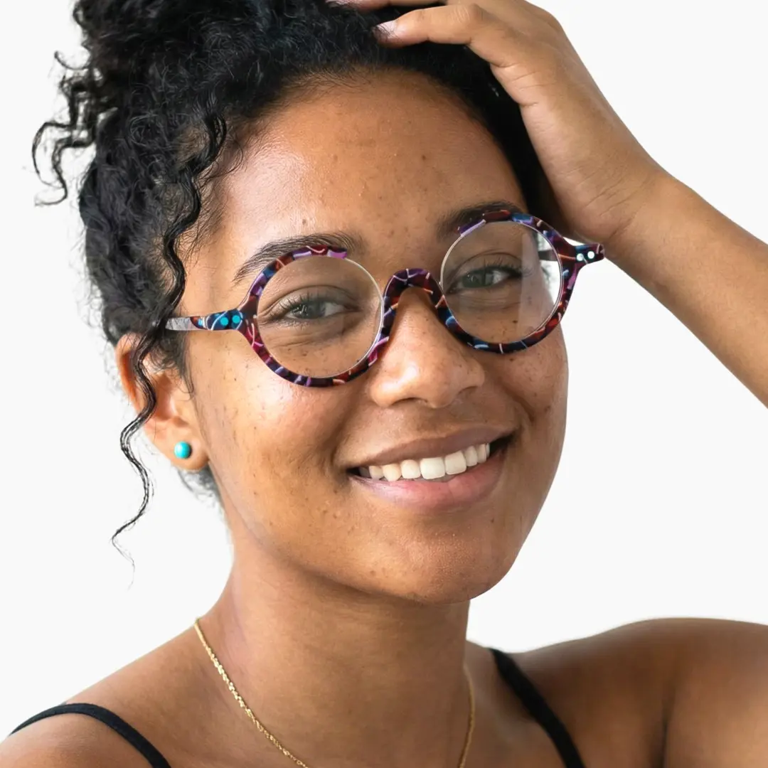 Slightly angled view of female wearing red tortoise round eyeglasses, hand in hair, smiling, RA0022212