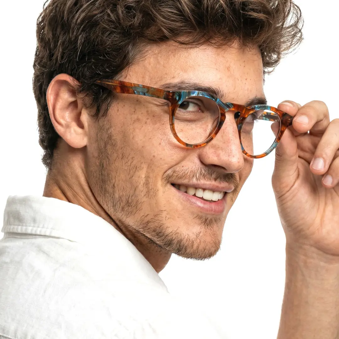 Profile view of male wearing colorful orange round eyeglasses, holding glasses, friendly smile, RA0032303