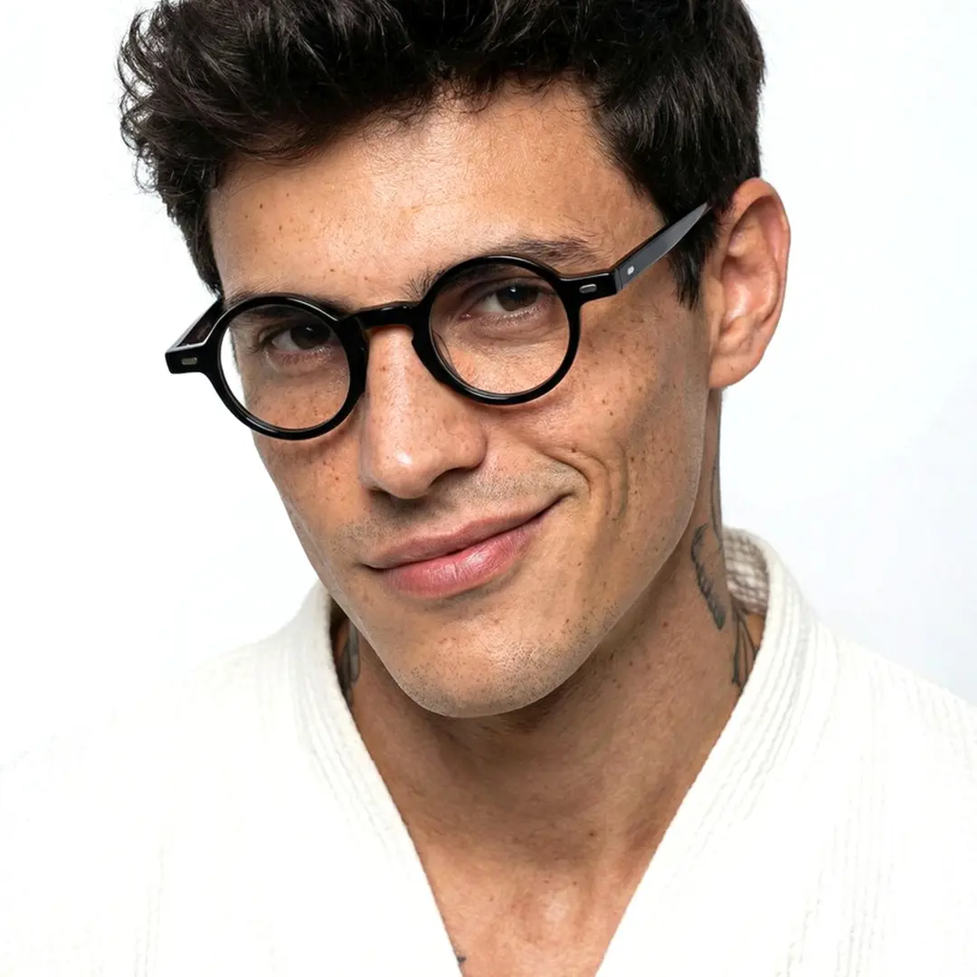 Front view of male wearing vintage black round eyeglasses, tilting head, smiling, RA0042301