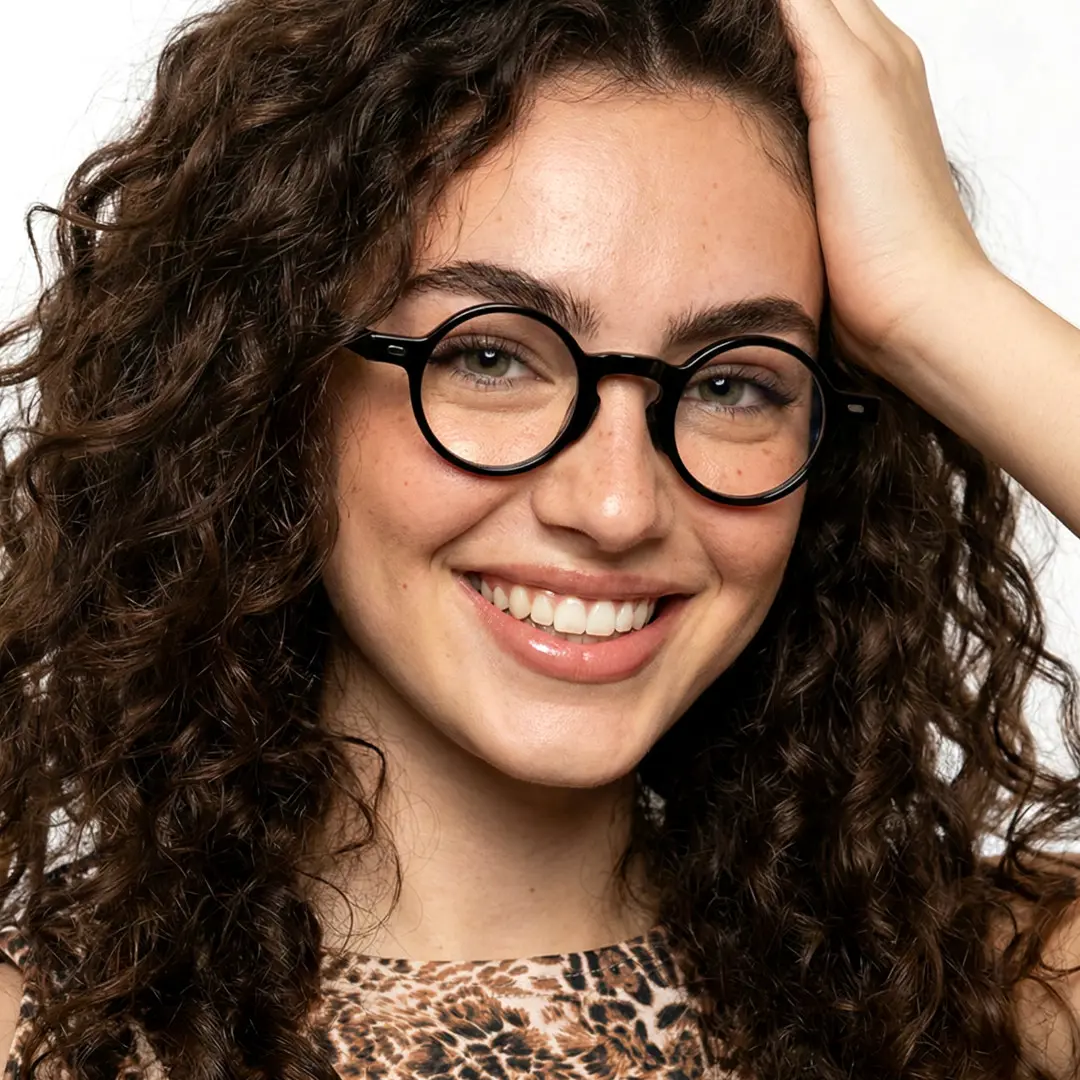 Front view of female wearing vintage black round eyeglasses, hand in hair, smiling, RA0042301