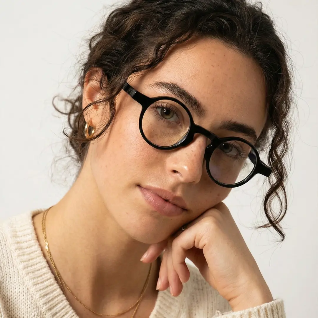 Front view of female wearing black round eyeglasses, resting chin on hand, neutral expression, RA0042303