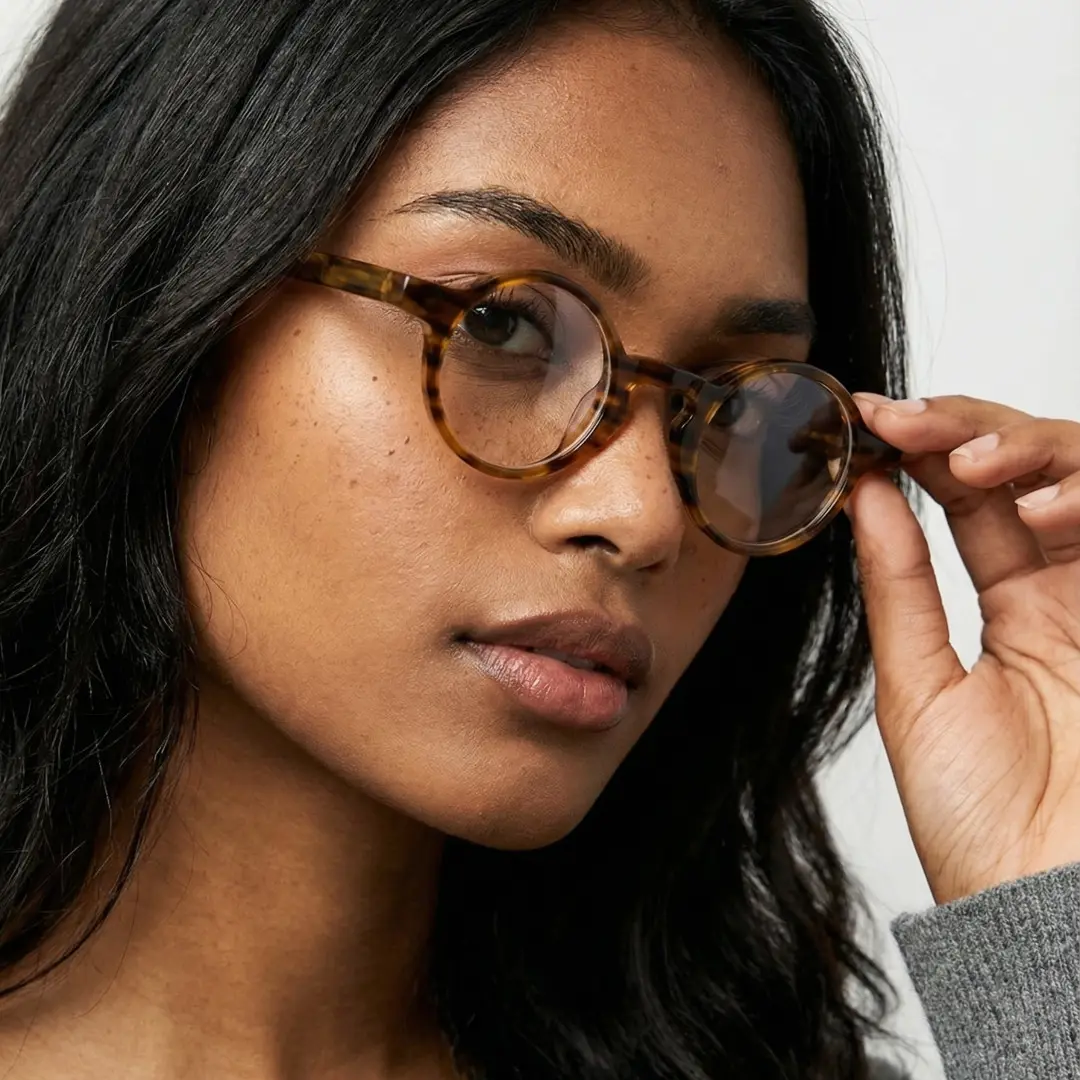 Three-quarter view of female wearing yellow tortoise round eyeglasses, touching frame, relaxed expression, RA0042303