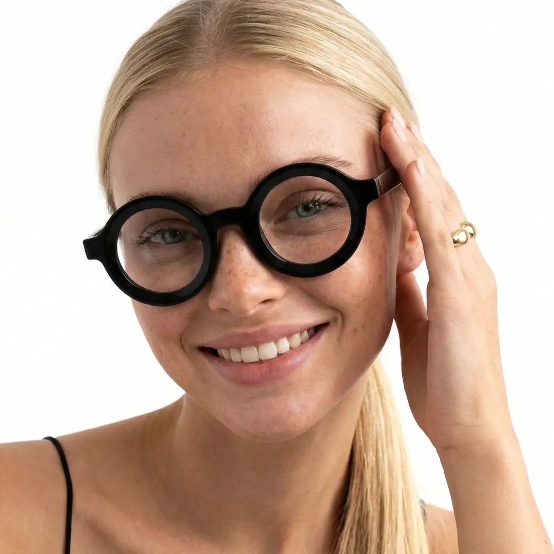 Front view of female wearing black round eyeglasses, hand near face, natural smile, RA0052408