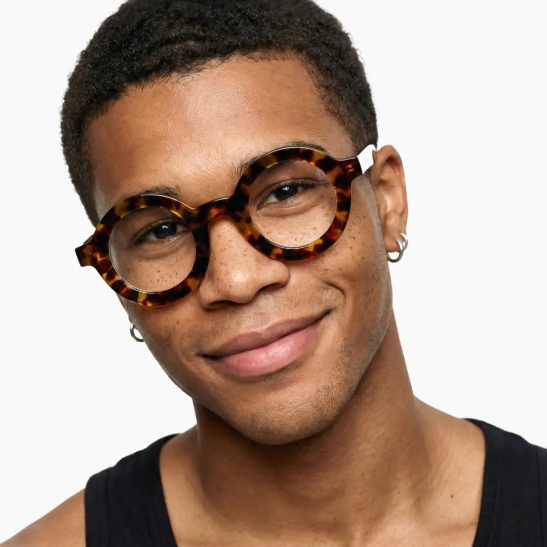 Front view of male wearing tortoise round eyeglasses, tilting head, natural smile, RA0052408