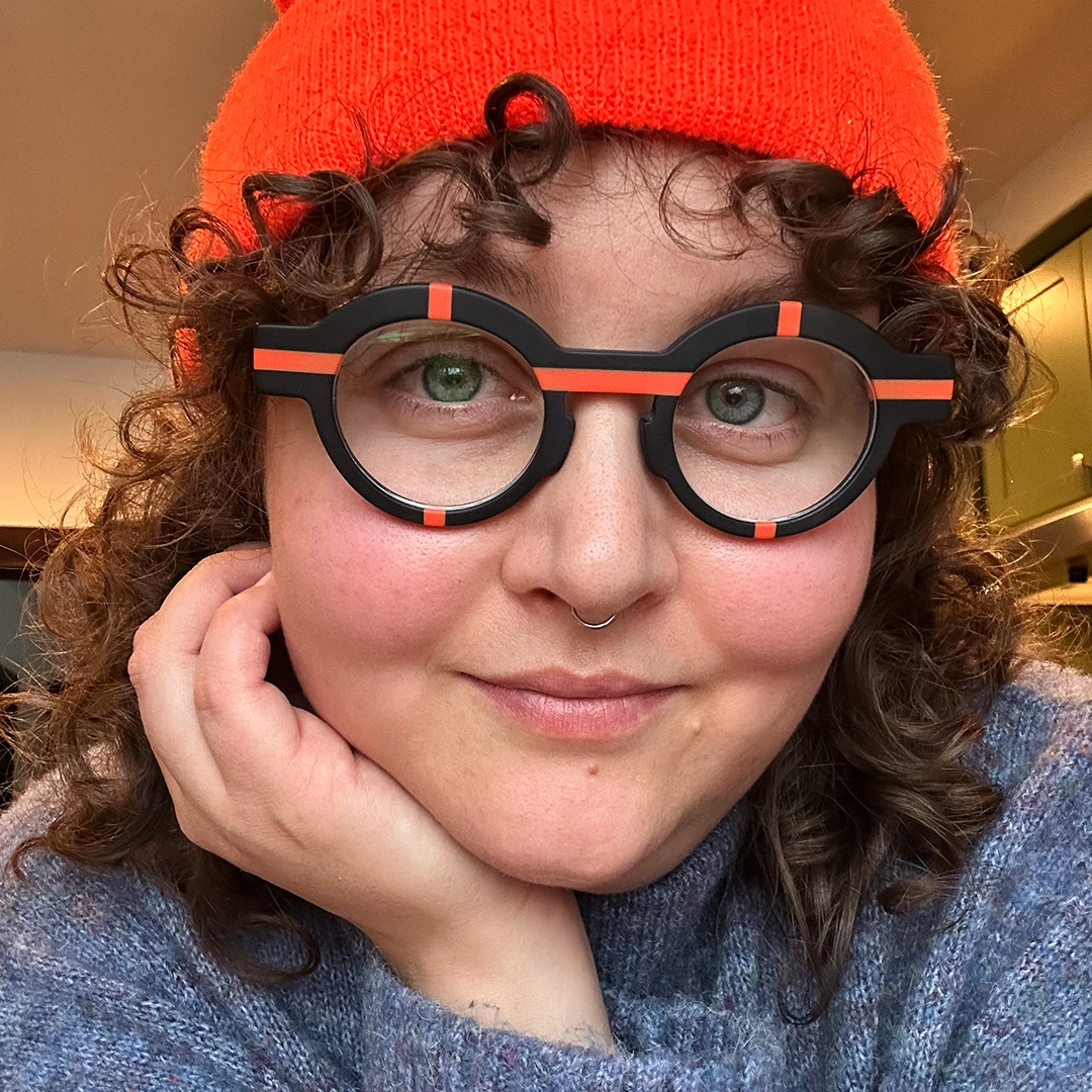 Front view of female wearing colorful black round eyeglasses, resting chin on hand, natural smile, RA0062311