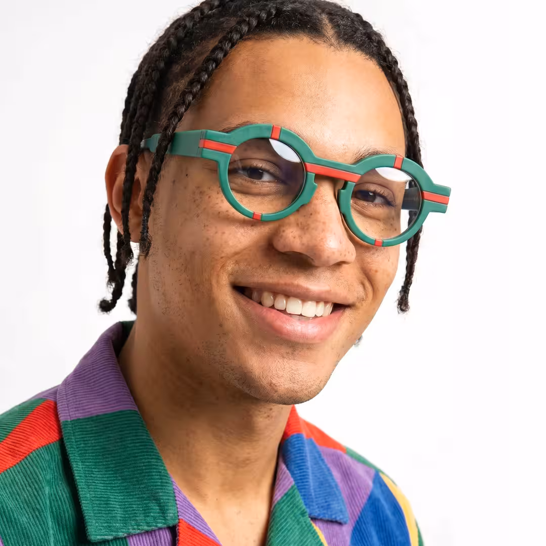 Three-quarter view of male wearing colorful green round eyeglasses, smiling, RA0062311