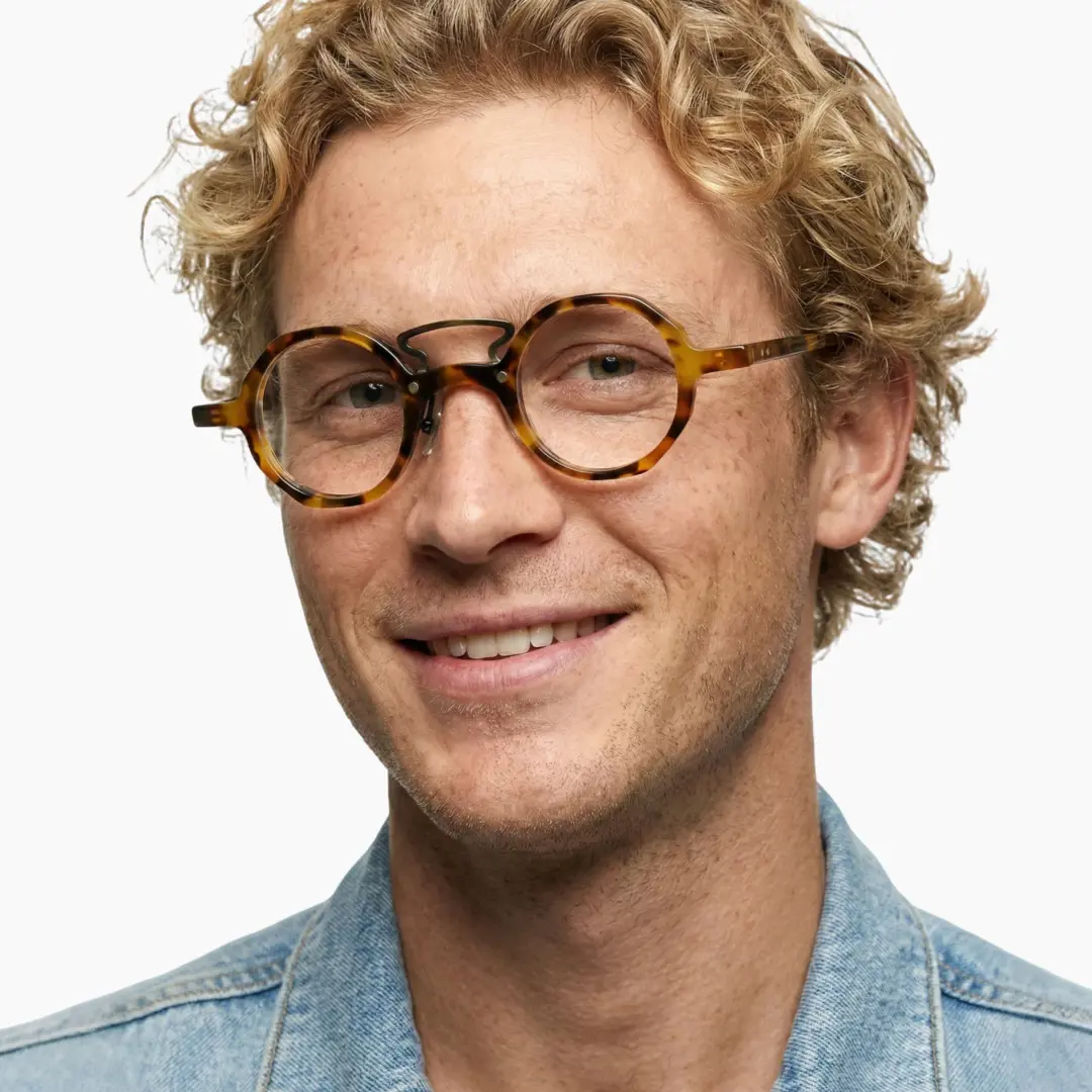 Three-quarter view of male wearing tortoise round eyeglasses, natural smile, RA0092305
