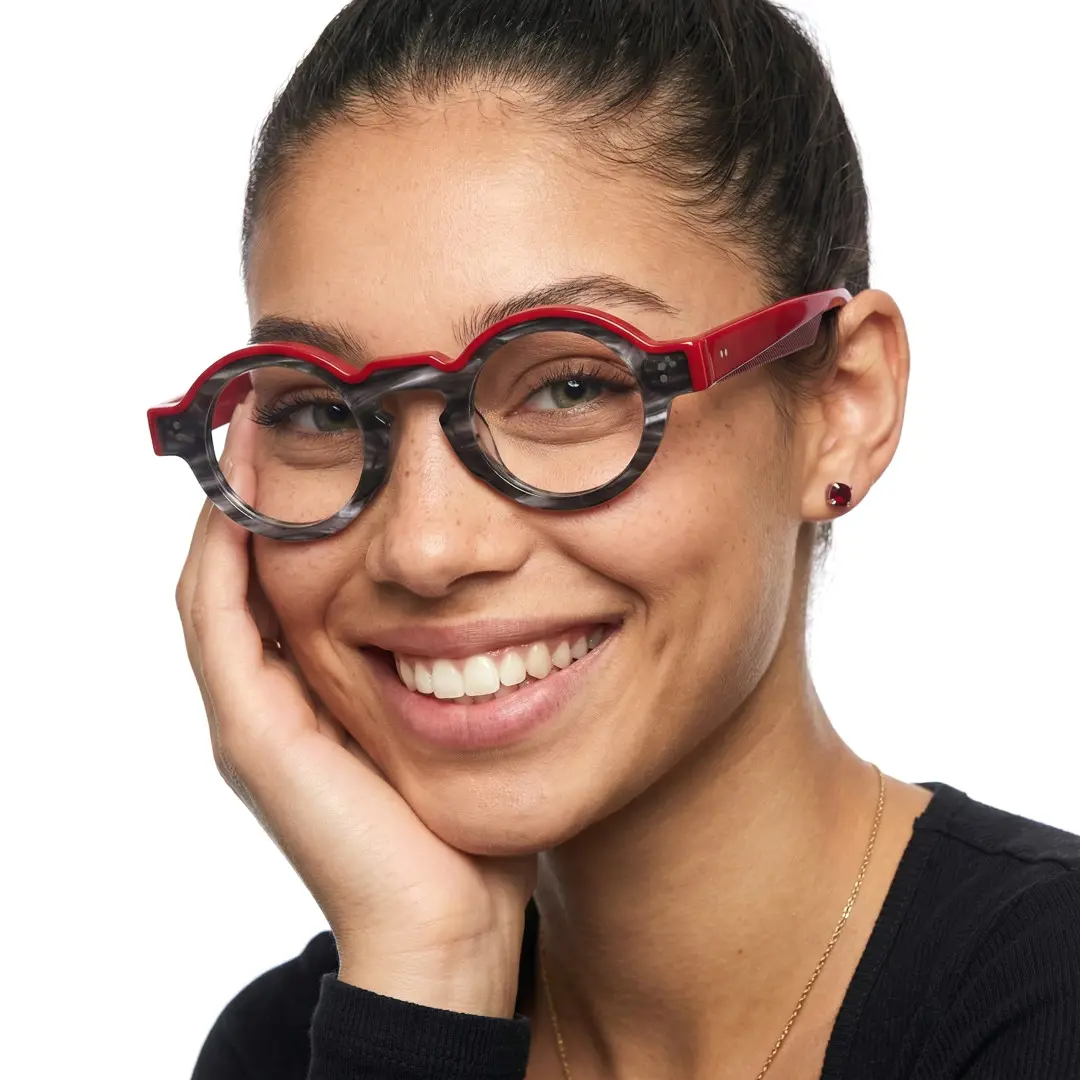 Three-quarter view of female wearing colorful black round eyeglasses, resting chin on hand, natural smile, RA0152406