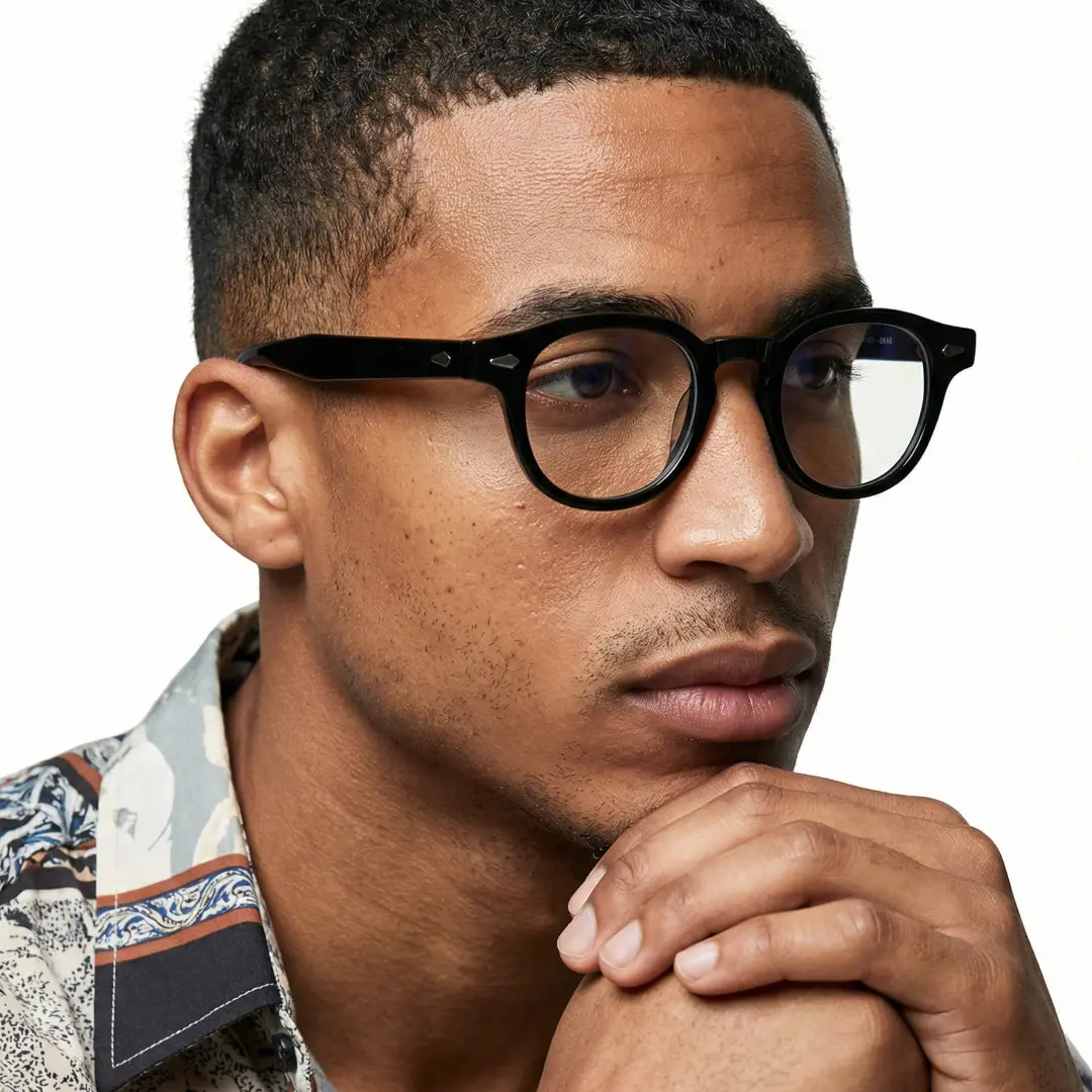 Three-quarter view of male wearing vintage black round eyeglasses, resting chin on hand, calm expression, RA0152411