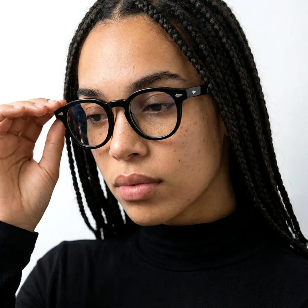 Front view of female wearing vintage black round eyeglasses, touching frame, thoughtful expression, RA0152411
