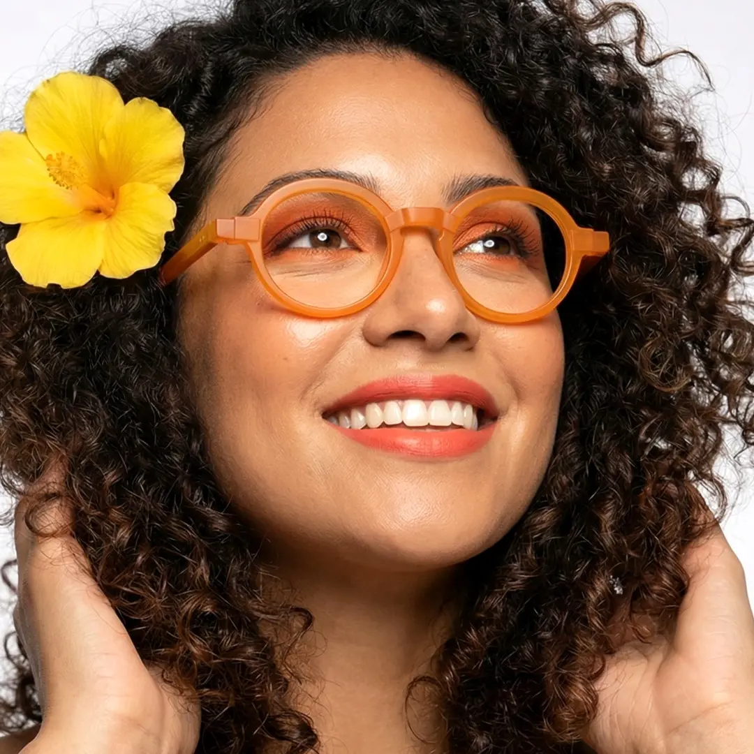 Face close-up view of female wearing colorful orange round eyeglasses, hand in hair, smiling, RA0182408