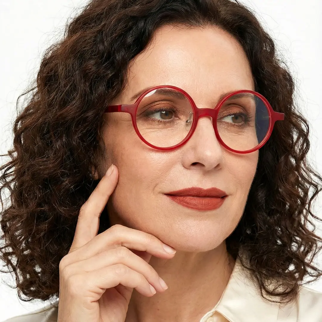 Three-quarter view of female wearing colorful red round eyeglasses, hand near face, neutral expression, RA0222310