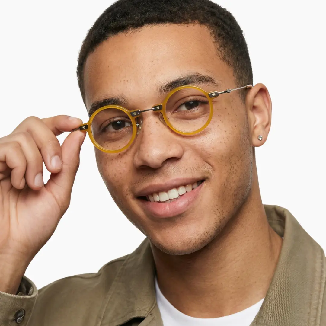 Three-quarter view of male wearing steampunk yellow round eyeglasses, holding glasses, smiling, RA0282411