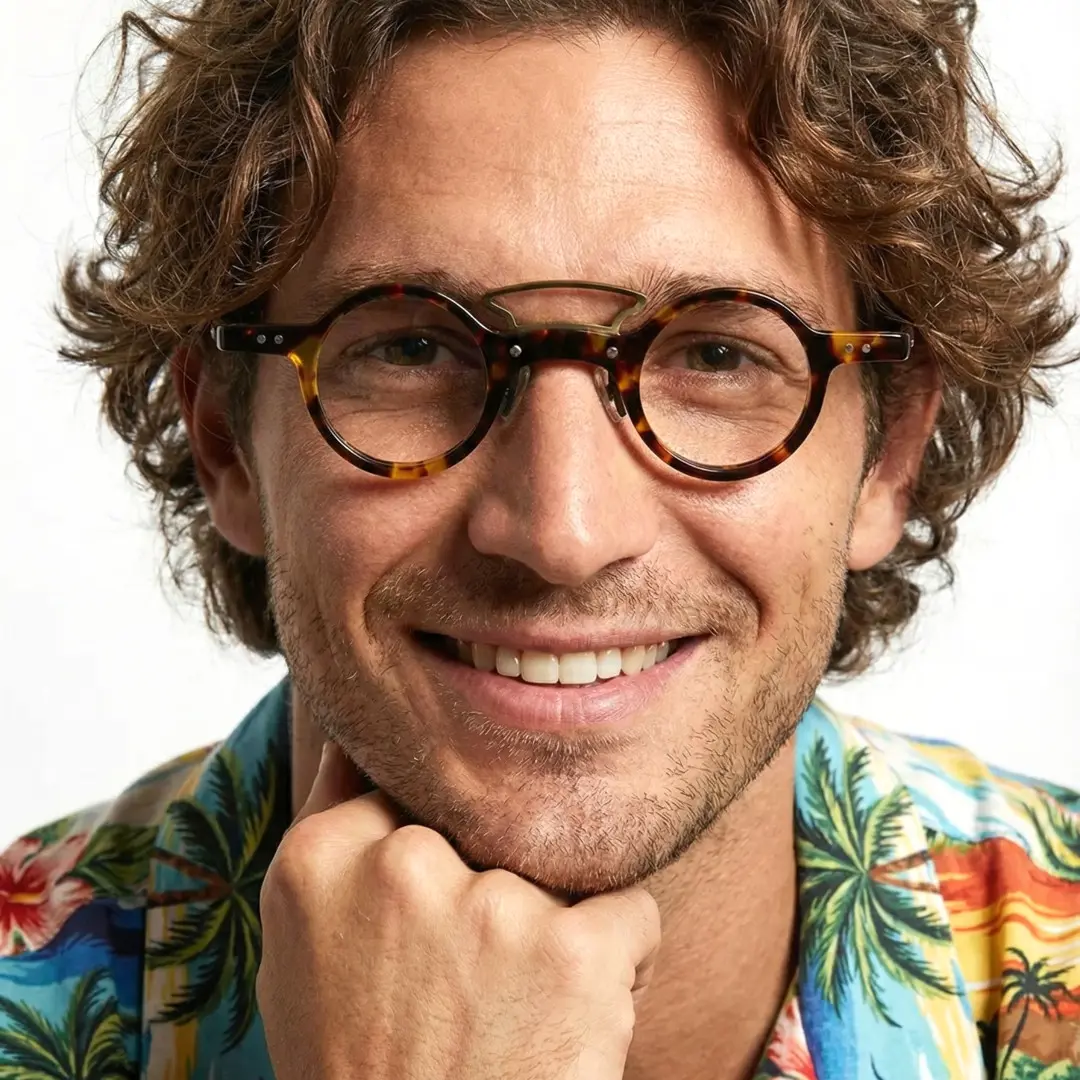 Straight-on view of male wearing tortoise round eyeglasses, resting chin on hand, natural smile, RA0302310