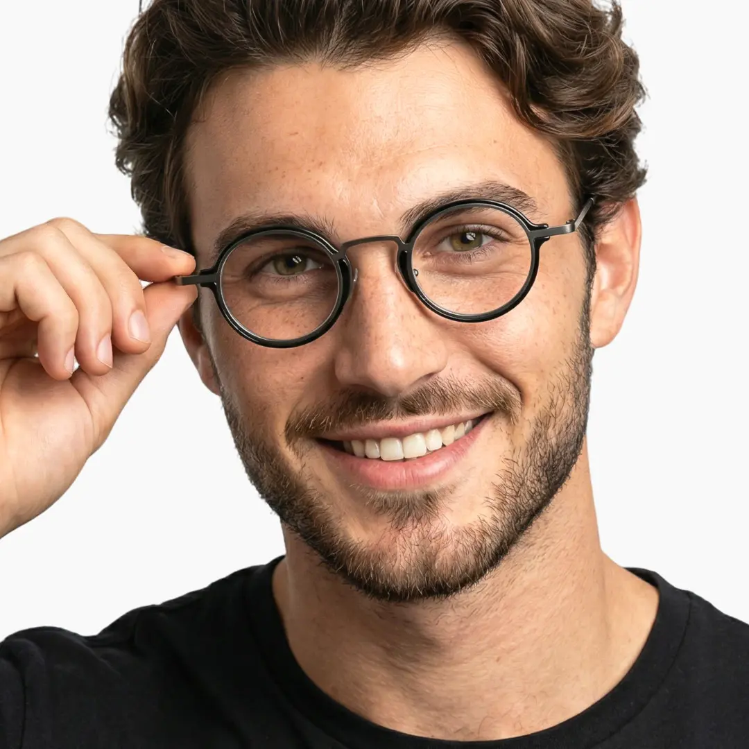 Slightly angled view of male wearing silver round eyeglasses, holding glasses, natural smile, RA0302402