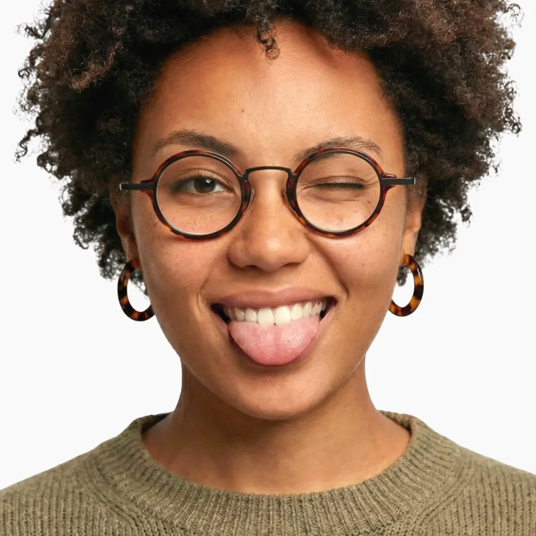 Front view of female wearing tortoise round eyeglasses, sticking out tongue, confident expression, RA0302402