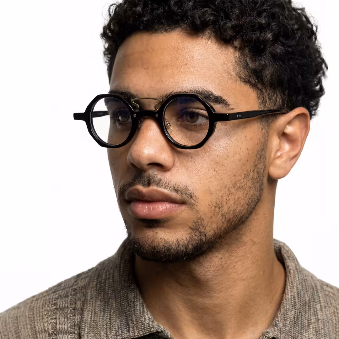 Male wearing vintage black round acetate eyeglasses, maintaining a neutral expression while looking away. SPU: RA0302411