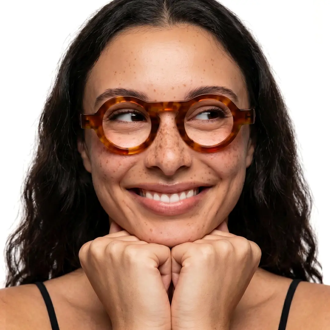 Front view of female wearing vintage yellow tortoise round eyeglasses, resting chin on hand, smiling, RA0312411