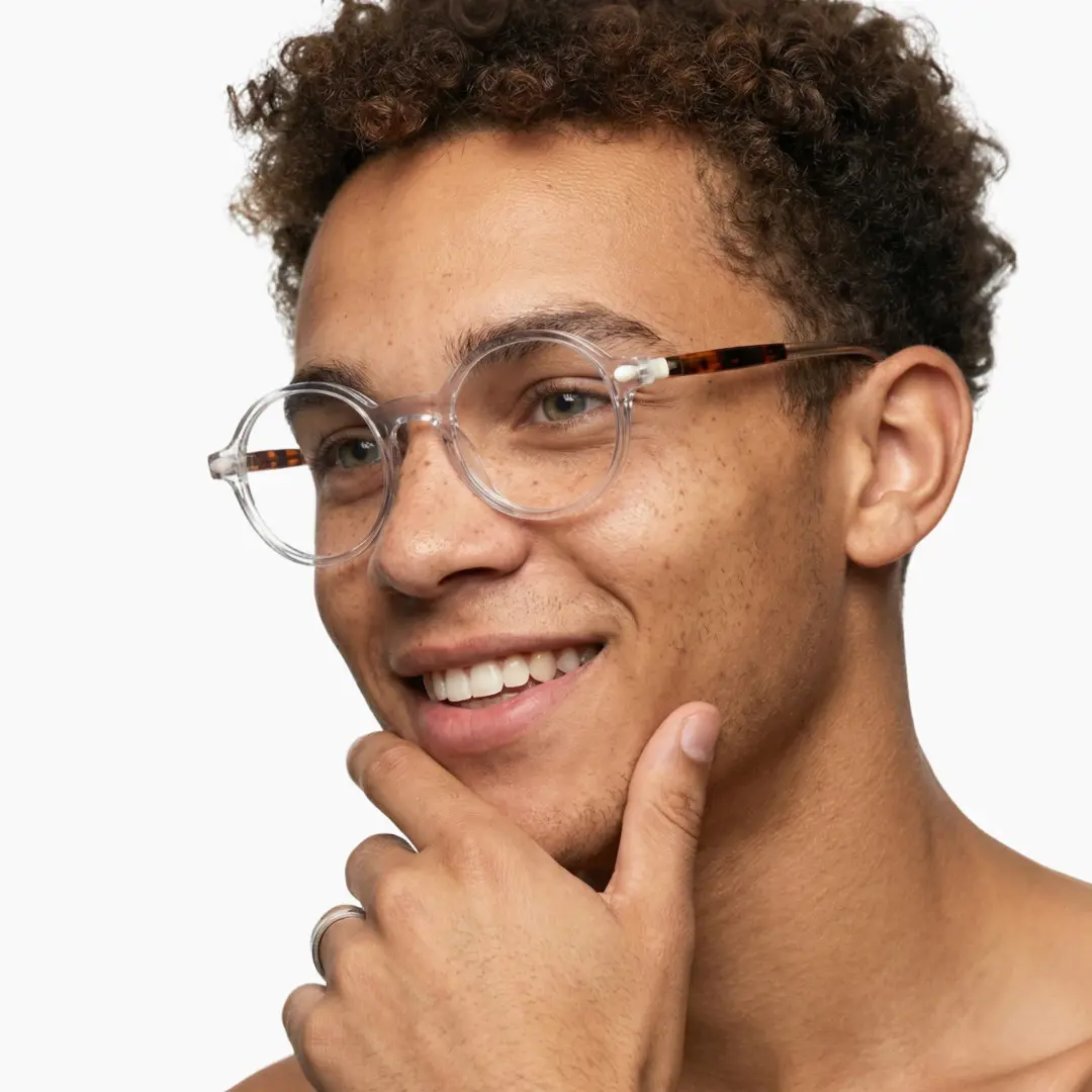 Three-quarter view of male wearing clear round eyeglasses, hand near face, natural smile, RA0312504