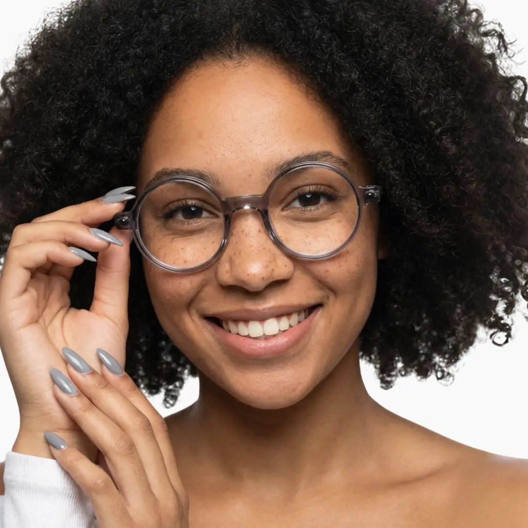 Front view of female wearing grey round eyeglasses, hand near face, smiling, RA0312504