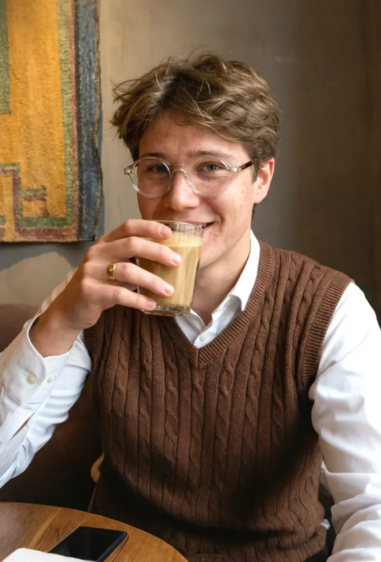 Male model wearing everyday clear round acetate eyeglasses inside a warm cozy cafe while holding a coffee glass. SPU: RA0312504