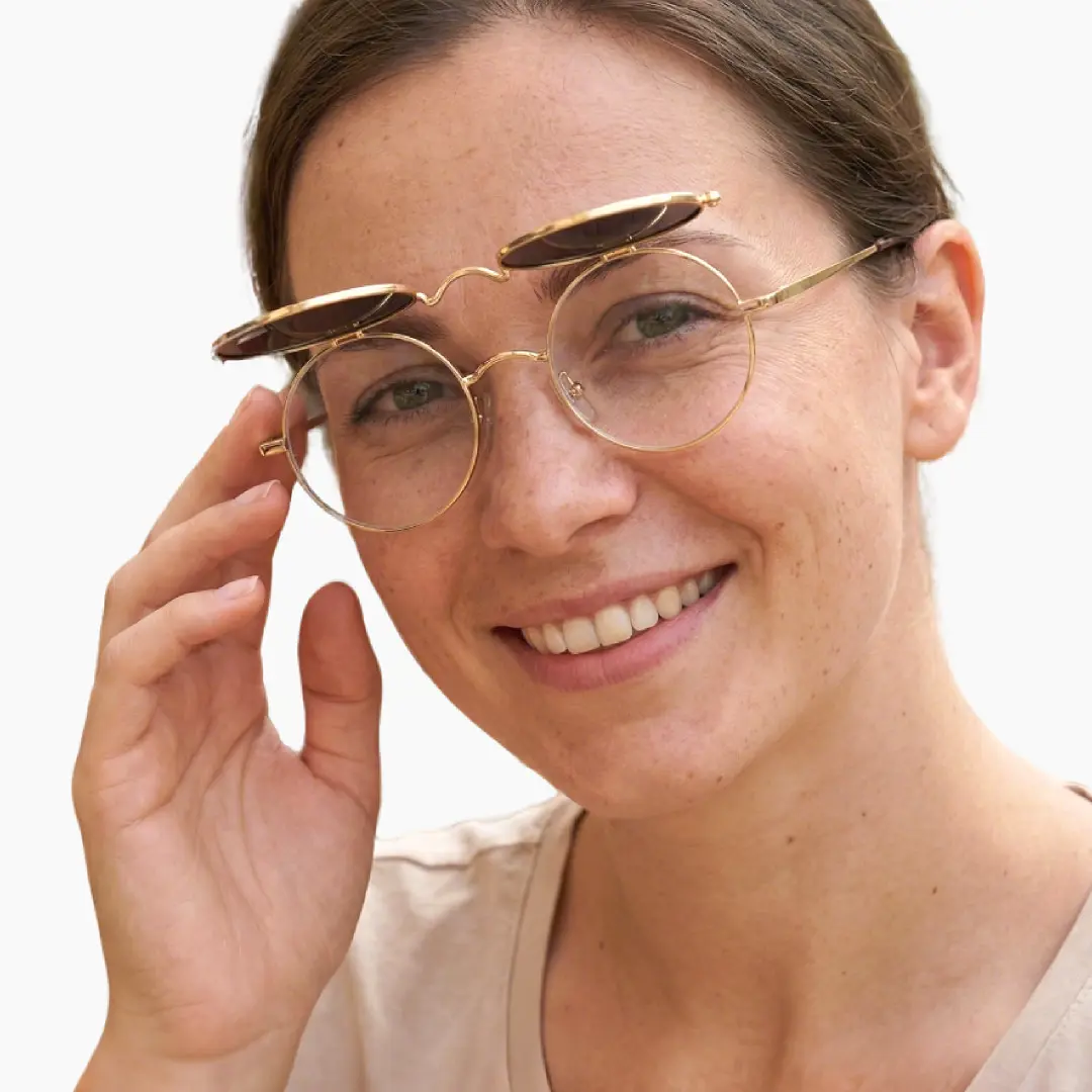 Profile view of female wearing gold round flip-up eyeglasses, touching frame, soft smile, RM0042601