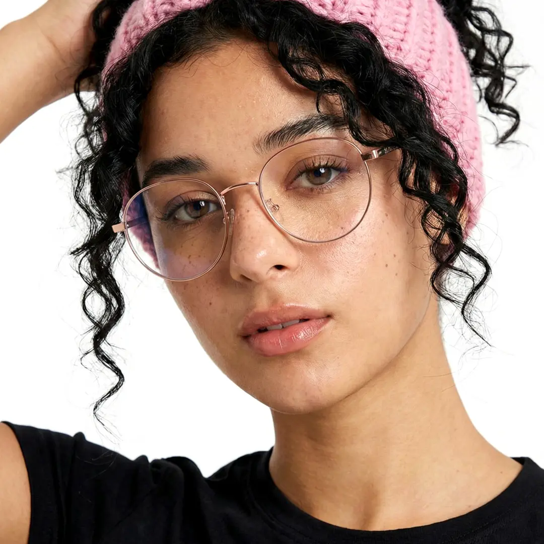 Slightly angled view of female wearing pink round eyeglasses, hand in hair, natural expression, RM0082209