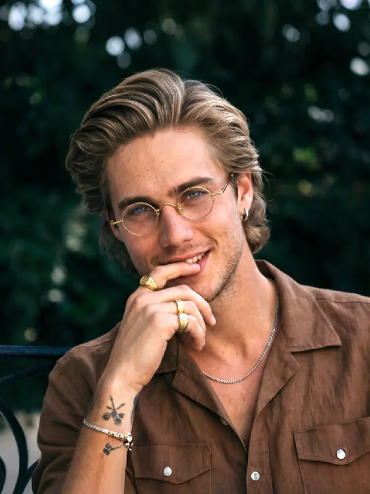Male model wearing john lennon gold round metal eyeglasses outdoors in a tranquil garden surrounded. SPU: RM0082308
