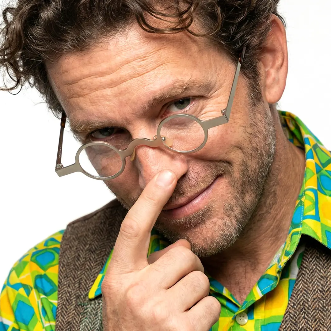 Tilted head view of male wearing silver round eyeglasses, glasses lowered, smiling, RM0122404