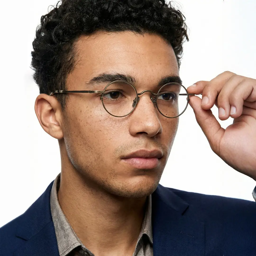 Three-quarter view of male wearing vintage bronze round eyeglasses, touching frame, calm expression, RM0242601
