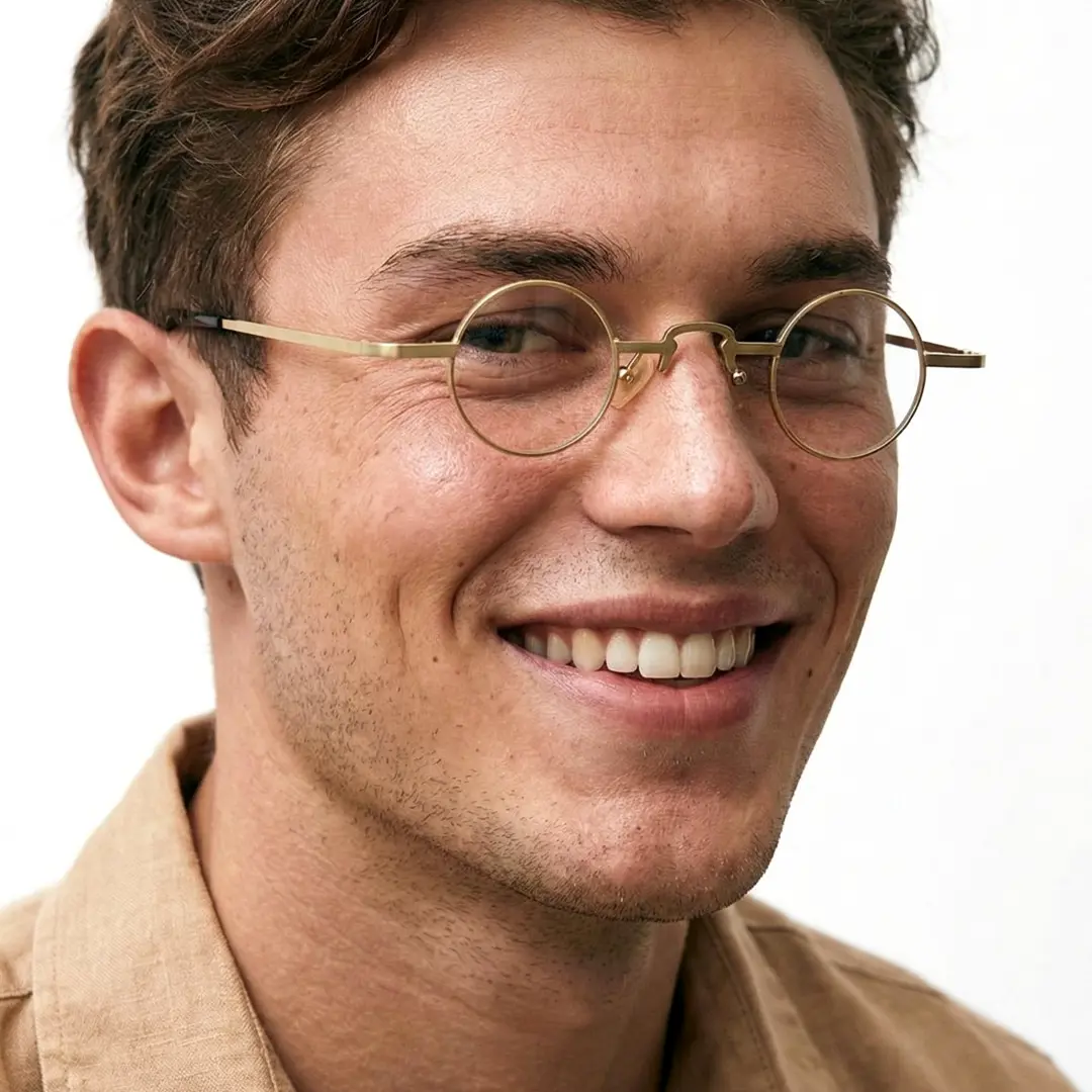 Slightly angled view of male wearing gold round eyeglasses, natural smile, RM0312412