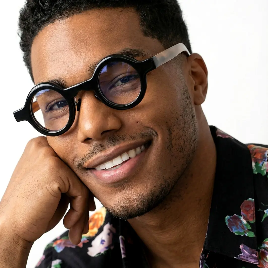 Three-quarter view of male wearing black round eyeglasses, resting chin on hand, smiling, RO0292511