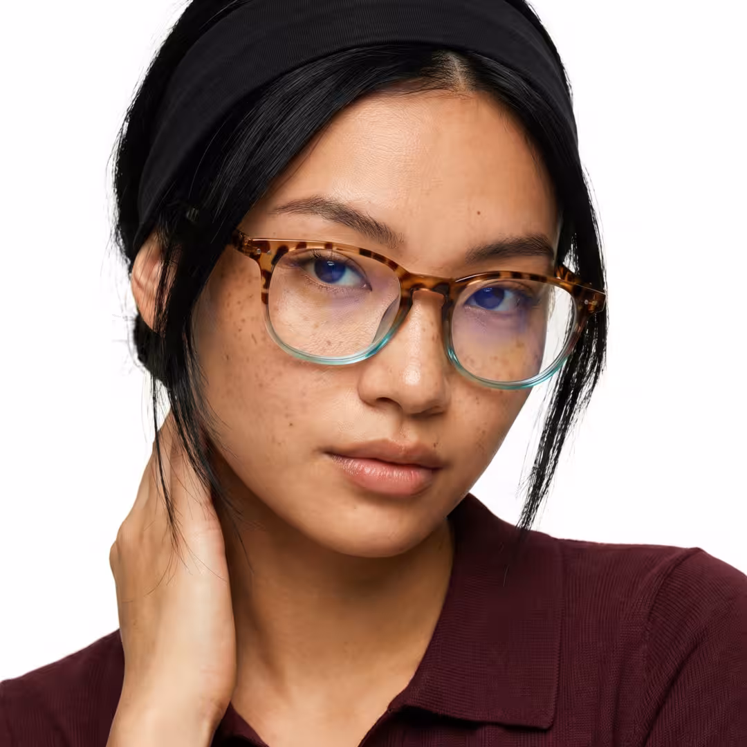 Female wearing two-tone round pc eyeglasses, slightly frowning while placing hand on neck. SPU: RP0052502