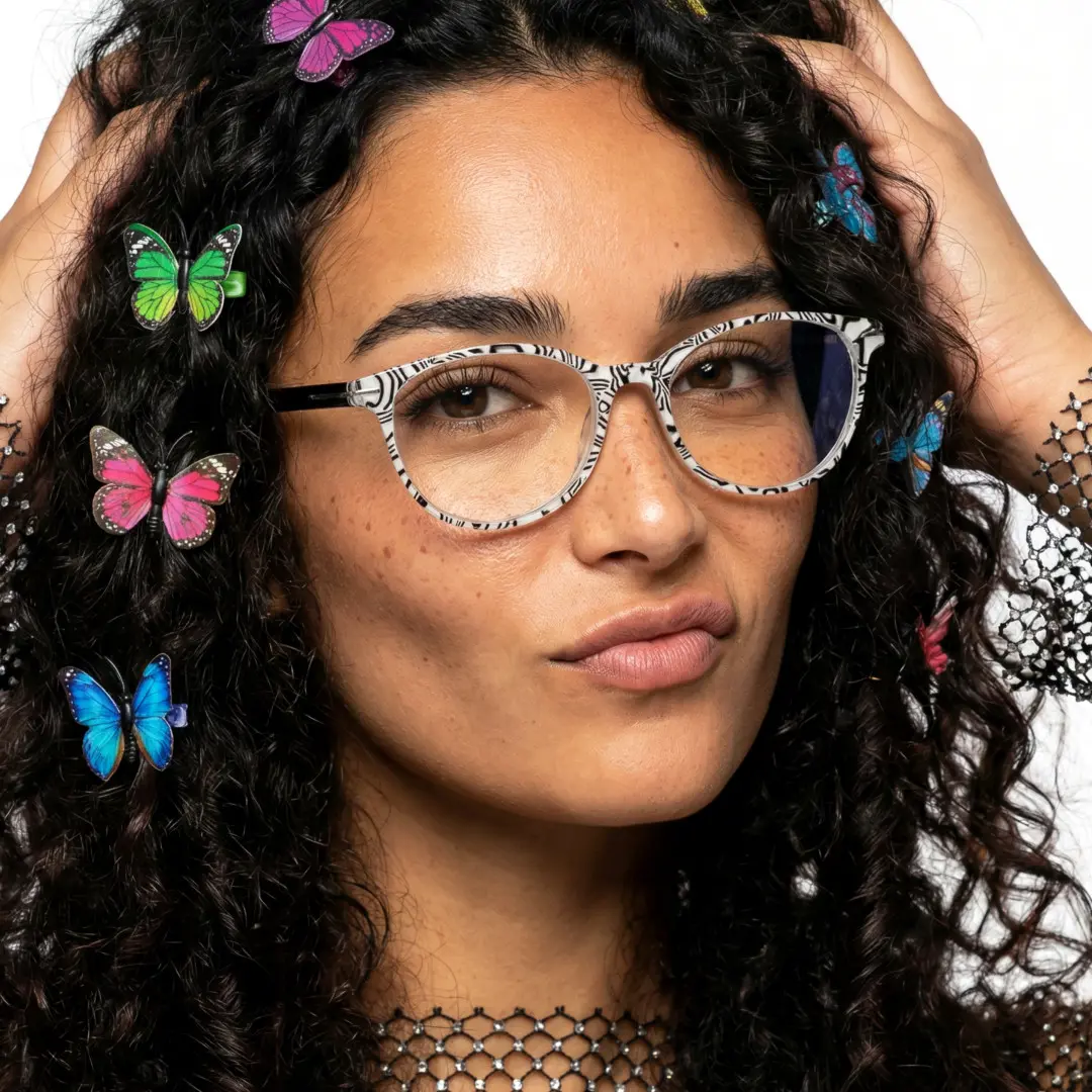 Three-quarter view of female wearing colorful black round eyeglasses, hand in hair, smiling, RP0212409