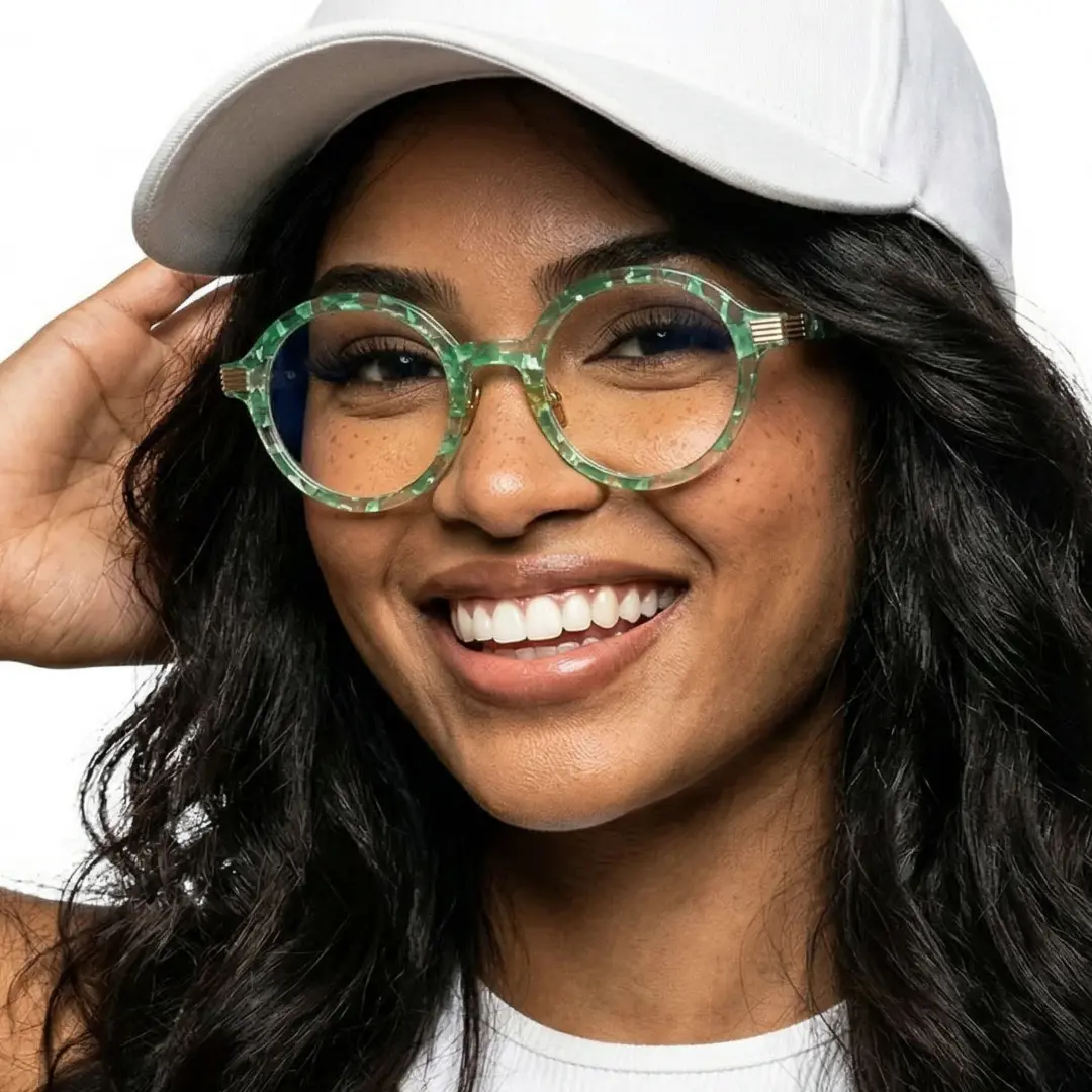 Three-quarter view of female wearing green round eyeglasses, hand in hair, smiling, RR0012303